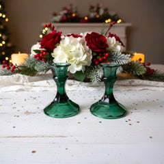 Pair of vintage Indiana Glass green candlestick holders with hexagonal bases, shown on a white surface. The emerald green glass catches the light, highlighting their faceted mid-century design and tapered silhouette. Ideal for holiday styling or eco-conscious vintage decor.