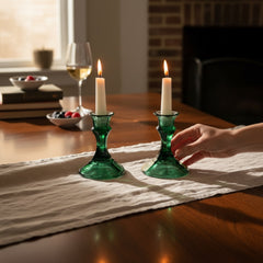 Pair of vintage Indiana Glass green candlestick holders with hexagonal bases, shown on a white surface. The emerald green glass catches the light, highlighting their faceted mid-century design and tapered silhouette. Ideal for holiday styling or eco-conscious vintage decor.