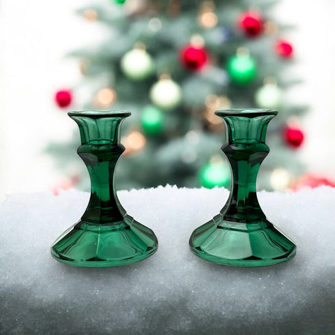 Pair of vintage Indiana Glass green candlestick holders with hexagonal bases, shown on a white surface. The emerald green glass catches the light, highlighting their faceted mid-century design and tapered silhouette. Ideal for holiday styling or eco-conscious vintage decor.