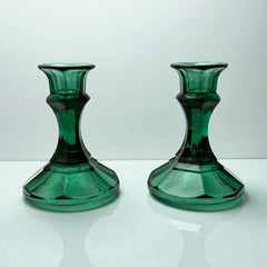 Pair of vintage Indiana Glass green candlestick holders with hexagonal bases, shown on a white surface. The emerald green glass catches the light, highlighting their faceted mid-century design and tapered silhouette. Ideal for holiday styling or eco-conscious vintage decor.