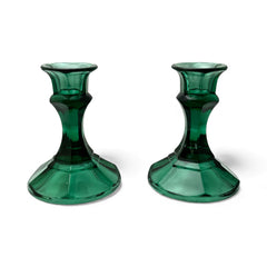 Pair of vintage Indiana Glass green candlestick holders with hexagonal bases, shown on a white surface. The emerald green glass catches the light, highlighting their faceted mid-century design and tapered silhouette. Ideal for holiday styling or eco-conscious vintage decor.