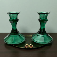 Pair of vintage Indiana Glass green candlestick holders with hexagonal bases, shown on a white surface. The emerald green glass catches the light, highlighting their faceted mid-century design and tapered silhouette. Ideal for holiday styling or eco-conscious vintage decor.