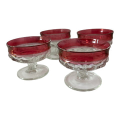 Set of vintage Indiana Glass cranberry sherbet glasses with thumbprint detailing, styled with soft lighting and floral accents to highlight their color, texture, and collectible charm.