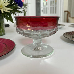 Set of vintage Indiana Glass cranberry sherbet glasses with thumbprint detailing, styled with soft lighting and floral accents to highlight their color, texture, and collectible charm.