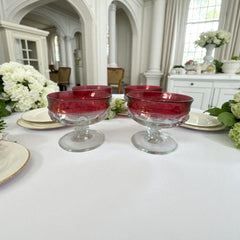 Set of vintage Indiana Glass cranberry sherbet glasses with thumbprint detailing, styled with soft lighting and floral accents to highlight their color, texture, and collectible charm.