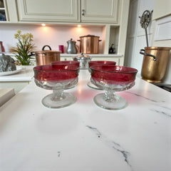Set of vintage Indiana Glass cranberry sherbet glasses with thumbprint detailing, styled with soft lighting and floral accents to highlight their color, texture, and collectible charm.