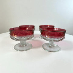 Set of vintage Indiana Glass cranberry sherbet glasses with thumbprint detailing, styled with soft lighting and floral accents to highlight their color, texture, and collectible charm.