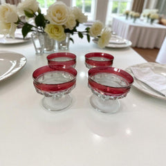 Set of vintage Indiana Glass cranberry sherbet glasses with thumbprint detailing, styled with soft lighting and floral accents to highlight their color, texture, and collectible charm.