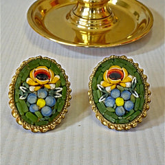 Vintage oval Italian micro‑mosaic clip‑on earrings with yellow and blue floral designs on a green background, framed in a gold‑tone twisted rope border. The mosaic is intact and detailed, with light wear visible on the backs.