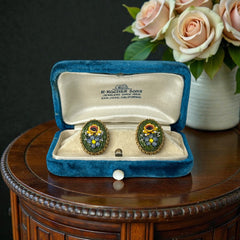 Vintage oval Italian micro‑mosaic clip‑on earrings with yellow and blue floral designs on a green background, framed in a gold‑tone twisted rope border. The mosaic is intact and detailed, with light wear visible on the backs.