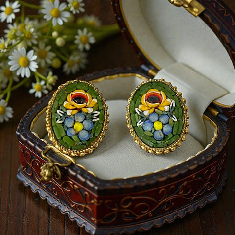 Vintage oval Italian micro‑mosaic clip‑on earrings with yellow and blue floral designs on a green background, framed in a gold‑tone twisted rope border. The mosaic is intact and detailed, with light wear visible on the backs.