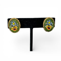 Vintage oval Italian micro‑mosaic clip‑on earrings with yellow and blue floral designs on a green background, framed in a gold‑tone twisted rope border. The mosaic is intact and detailed, with light wear visible on the backs.