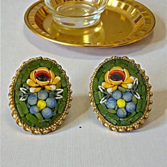 Vintage oval Italian micro‑mosaic clip‑on earrings with yellow and blue floral designs on a green background, framed in a gold‑tone twisted rope border. The mosaic is intact and detailed, with light wear visible on the backs.