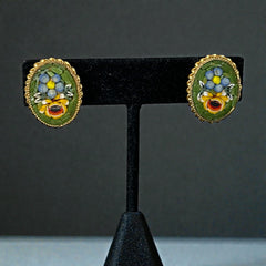 Vintage oval Italian micro‑mosaic clip‑on earrings with yellow and blue floral designs on a green background, framed in a gold‑tone twisted rope border. The mosaic is intact and detailed, with light wear visible on the backs.