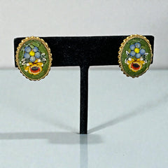 Vintage oval Italian micro‑mosaic clip‑on earrings with yellow and blue floral designs on a green background, framed in a gold‑tone twisted rope border. The mosaic is intact and detailed, with light wear visible on the backs.