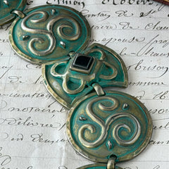 Close‑up of a vintage Ivar Hyden Celtic bracelet with round brass‑tone links, green patina, and a square hematite cabochon centerpiece.