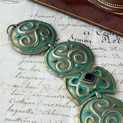 Close‑up of a vintage Ivar Hyden Celtic bracelet with round brass‑tone links, green patina, and a square hematite cabochon centerpiece.