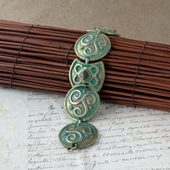 Close‑up of a vintage Ivar Hyden Celtic bracelet with round brass‑tone links, green patina, and a square hematite cabochon centerpiece.