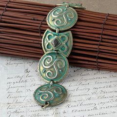 Close‑up of a vintage Ivar Hyden Celtic bracelet with round brass‑tone links, green patina, and a square hematite cabochon centerpiece.