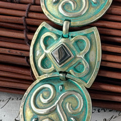 Close‑up of a vintage Ivar Hyden Celtic bracelet with round brass‑tone links, green patina, and a square hematite cabochon centerpiece.