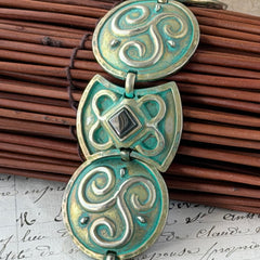 Close‑up of a vintage Ivar Hyden Celtic bracelet with round brass‑tone links, green patina, and a square hematite cabochon centerpiece.