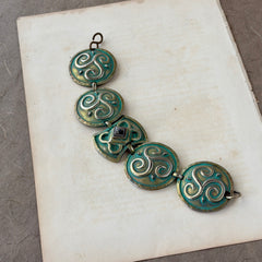 Close‑up of a vintage Ivar Hyden Celtic bracelet with round brass‑tone links, green patina, and a square hematite cabochon centerpiece.