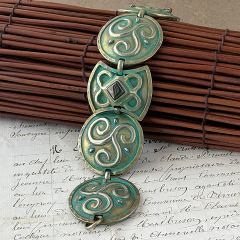 Close‑up of a vintage Ivar Hyden Celtic bracelet with round brass‑tone links, green patina, and a square hematite cabochon centerpiece.