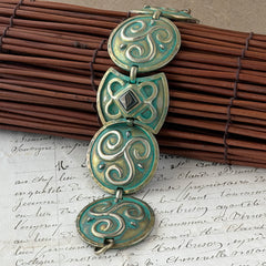 Close‑up of a vintage Ivar Hyden Celtic bracelet with round brass‑tone links, green patina, and a square hematite cabochon centerpiece.