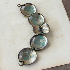 Close‑up of a vintage Ivar Hyden Celtic bracelet with round brass‑tone links, green patina, and a square hematite cabochon centerpiece.