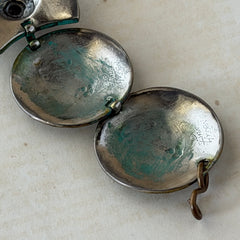 Close‑up of a vintage Ivar Hyden Celtic bracelet with round brass‑tone links, green patina, and a square hematite cabochon centerpiece.