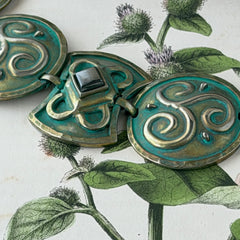 Close‑up of a vintage Ivar Hyden Celtic bracelet with round brass‑tone links, green patina, and a square hematite cabochon centerpiece.