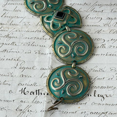 Close‑up of a vintage Ivar Hyden Celtic bracelet with round brass‑tone links, green patina, and a square hematite cabochon centerpiece.