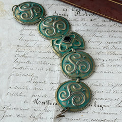 Close‑up of a vintage Ivar Hyden Celtic bracelet with round brass‑tone links, green patina, and a square hematite cabochon centerpiece.