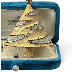 Vintage JJ Christmas tree brooch in textured gold-tone metal with silver-tone garlands paved in clear rhinestones and a red star at the top; signed JJ with copyright mark on the back, typical of 1980s holiday jewelry.