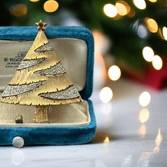 Vintage JJ Christmas tree brooch in textured gold-tone metal with silver-tone garlands paved in clear rhinestones and a red star at the top; signed JJ with copyright mark on the back, typical of 1980s holiday jewelry.