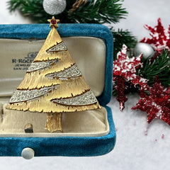 Vintage JJ Christmas tree brooch in textured gold-tone metal with silver-tone garlands paved in clear rhinestones and a red star at the top; signed JJ with copyright mark on the back, typical of 1980s holiday jewelry.