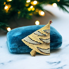 Vintage JJ Christmas tree brooch in textured gold-tone metal with silver-tone garlands paved in clear rhinestones and a red star at the top; signed JJ with copyright mark on the back, typical of 1980s holiday jewelry.