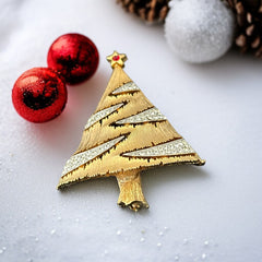 Vintage JJ Christmas tree brooch in textured gold-tone metal with silver-tone garlands paved in clear rhinestones and a red star at the top; signed JJ with copyright mark on the back, typical of 1980s holiday jewelry.