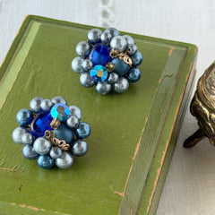 Vintage Japan blue faux pearl and rhinestone cluster clip‑on earrings with gold filigree backs, shown from multiple angles to highlight their wired construction and luminous beads.
