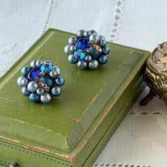 Vintage Japan blue faux pearl and rhinestone cluster clip‑on earrings with gold filigree backs, shown from multiple angles to highlight their wired construction and luminous beads.