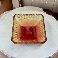 Vintage Jeannette Amberina Depression glass dish from the 1930s featuring a square footed base, an Acorn and Leaf pattern, and a color gradient from amber/yellow to red. Perfect as a candy dish or decorative piece, with a small chip on the rim adding character to its vintage charm.