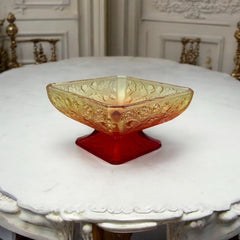 Vintage Jeannette Amberina Depression glass dish from the 1930s featuring a square footed base, an Acorn and Leaf pattern, and a color gradient from amber/yellow to red. Perfect as a candy dish or decorative piece, with a small chip on the rim adding character to its vintage charm.