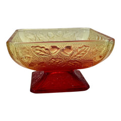 Vintage Jeannette Amberina Depression glass dish from the 1930s featuring a square footed base, an Acorn and Leaf pattern, and a color gradient from amber/yellow to red. Perfect as a candy dish or decorative piece, with a small chip on the rim adding character to its vintage charm.
