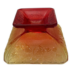Vintage Jeannette Amberina Depression glass dish from the 1930s featuring a square footed base, an Acorn and Leaf pattern, and a color gradient from amber/yellow to red. Perfect as a candy dish or decorative piece, with a small chip on the rim adding character to its vintage charm.