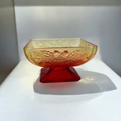 Vintage Jeannette Amberina Depression glass dish from the 1930s featuring a square footed base, an Acorn and Leaf pattern, and a color gradient from amber/yellow to red. Perfect as a candy dish or decorative piece, with a small chip on the rim adding character to its vintage charm.