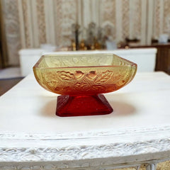 Vintage Jeannette Amberina Depression glass dish from the 1930s featuring a square footed base, an Acorn and Leaf pattern, and a color gradient from amber/yellow to red. Perfect as a candy dish or decorative piece, with a small chip on the rim adding character to its vintage charm.