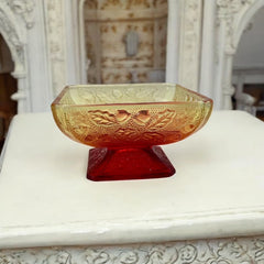 Vintage Jeannette Amberina Depression glass dish from the 1930s featuring a square footed base, an Acorn and Leaf pattern, and a color gradient from amber/yellow to red. Perfect as a candy dish or decorative piece, with a small chip on the rim adding character to its vintage charm.