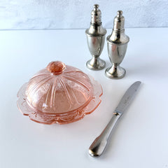Vintage Jeannette Cherry Blossom pink Depression glass butter dish with embossed floral pattern, scalloped edges, and domed lid, shown in natural light on a white tabletop.
