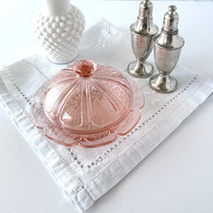 Vintage Jeannette Cherry Blossom pink Depression glass butter dish with embossed floral pattern, scalloped edges, and domed lid, shown in natural light on a white tabletop.