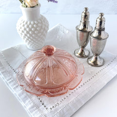 Vintage Jeannette Cherry Blossom pink Depression glass butter dish with embossed floral pattern, scalloped edges, and domed lid, shown in natural light on a white tabletop.